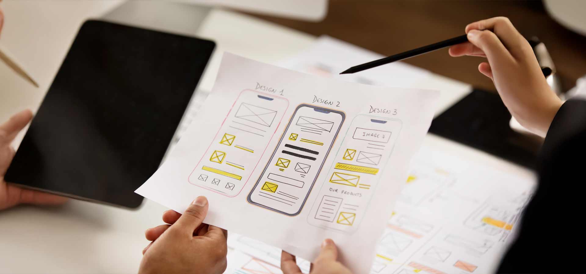 UI/UX team reviewing hand-drawn mobile app wireframes on paper